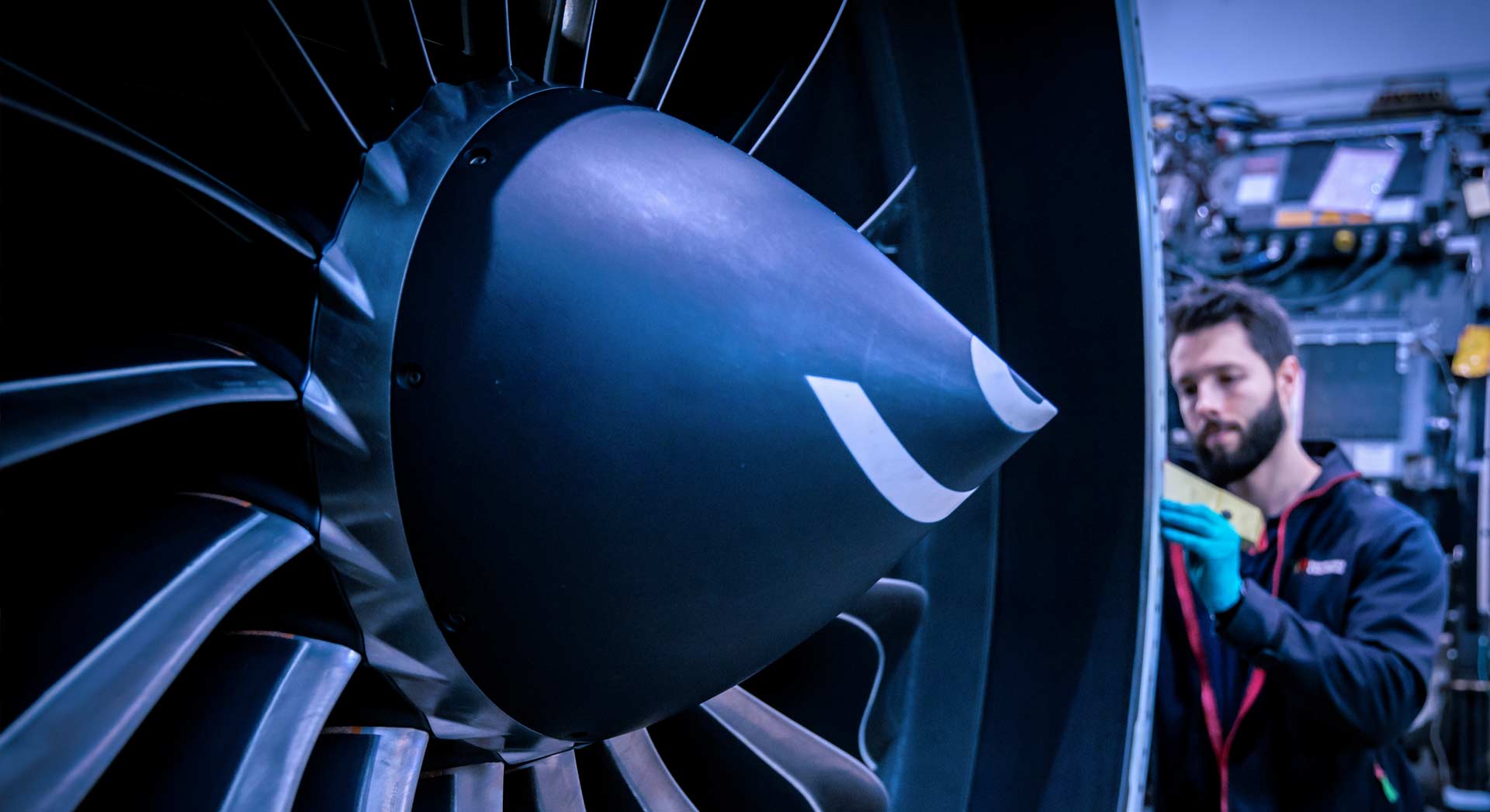 Close-up view of a jet engine fan blades and spinner cone. On the right, a TAP Maintenance worker handles engine components.
