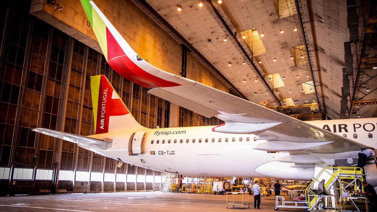 Airbus A330-900neo inside a large TAP aircraft hangar. The airplane is undergoing maintenance or inspection.