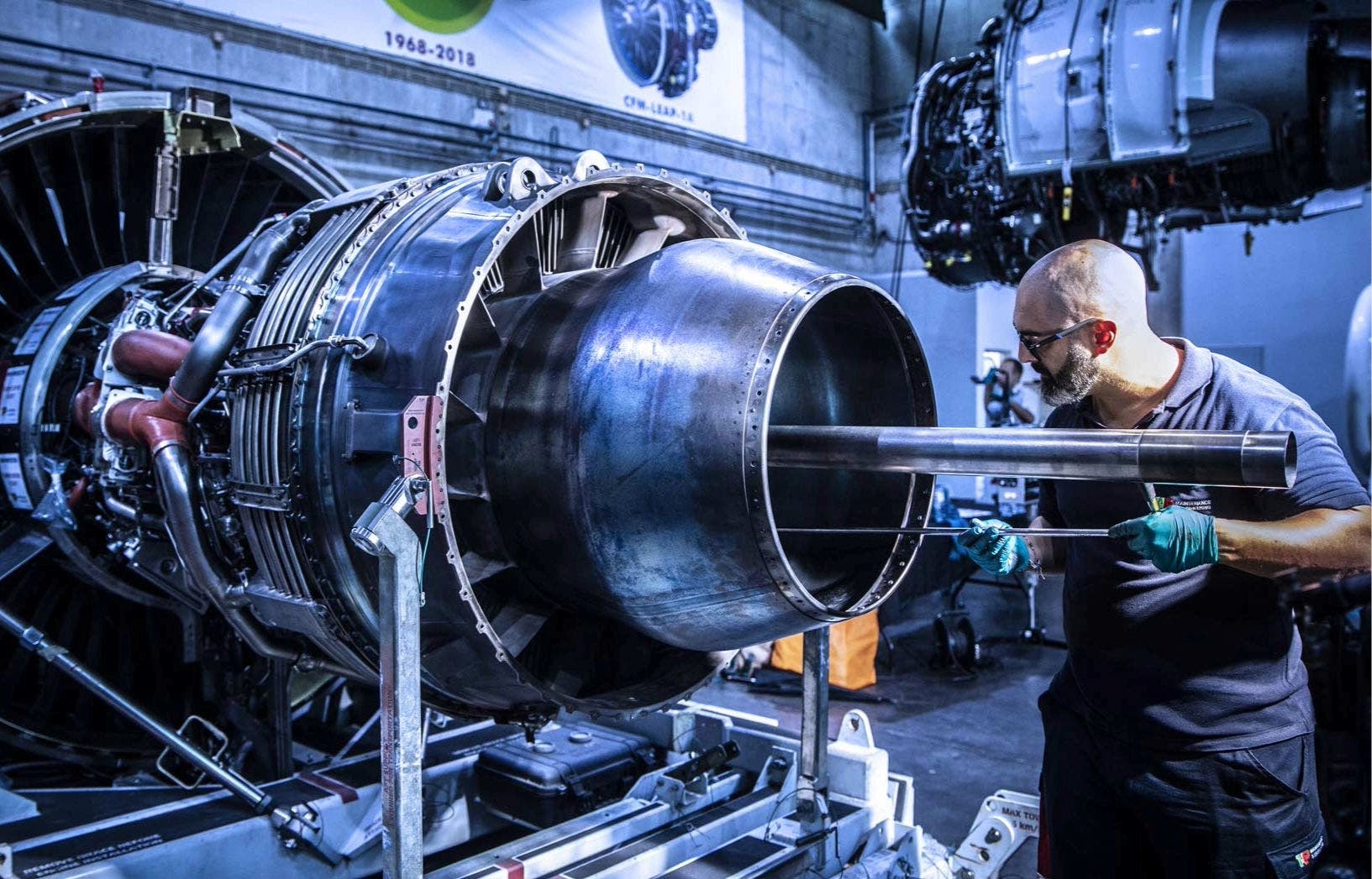 TAP Maintenance worker working on a large aircraft jet engine inside a maintenance facility.