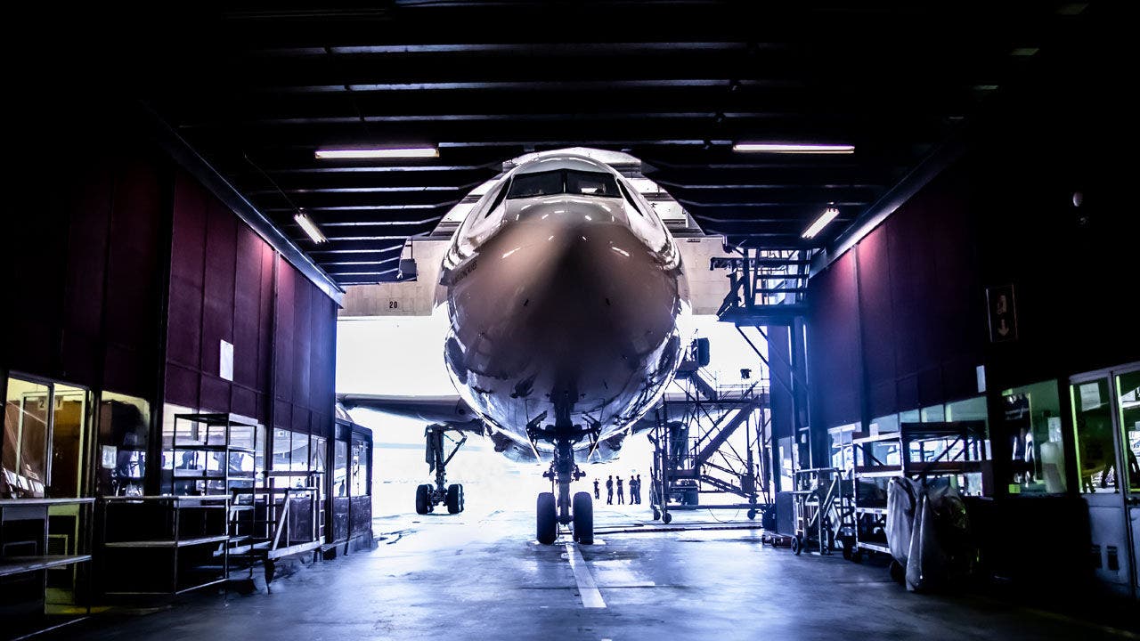 Front view of a commercial airplane inside a large maintenance hangar.