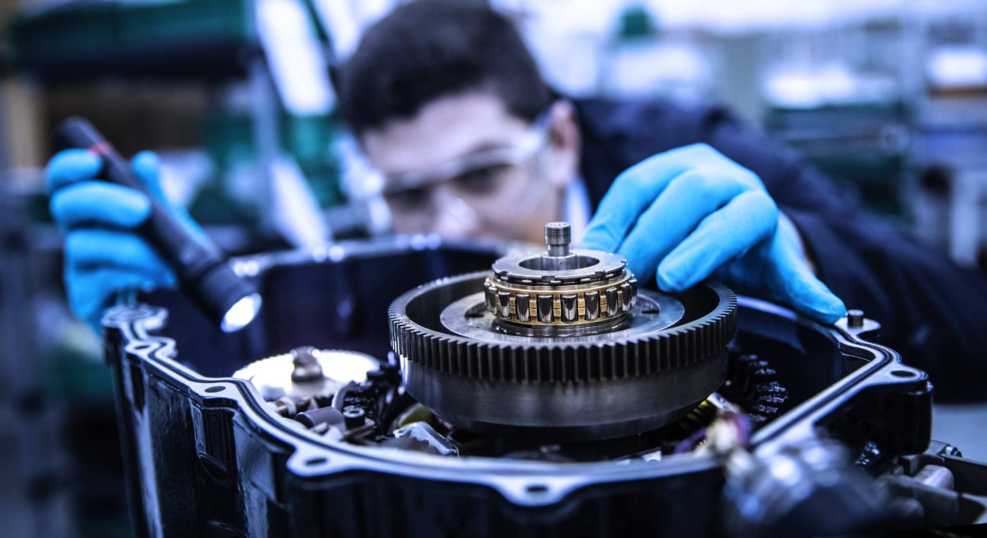 Close-up scene of a engineer inspecting a mechanical gear system. Person is wearing blue protective gloves and safety glasses.
