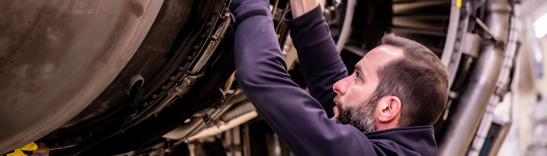 TAP Maintenance technician working on a jet engine during maintenance. He is wearing a dark blue uniform.