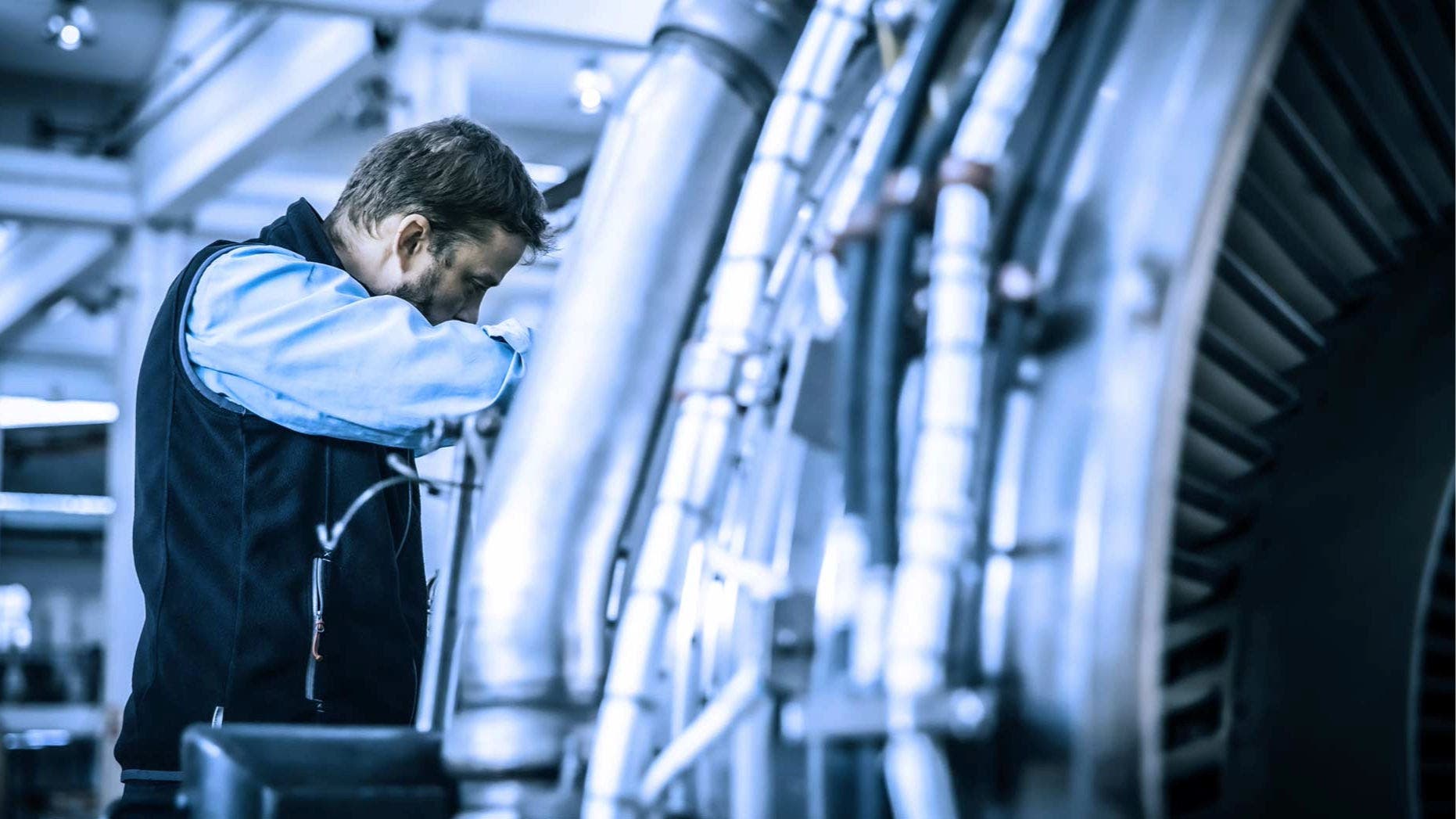 TAP Maintenance worker inspecting a large mechanical component, part of a jet engine.