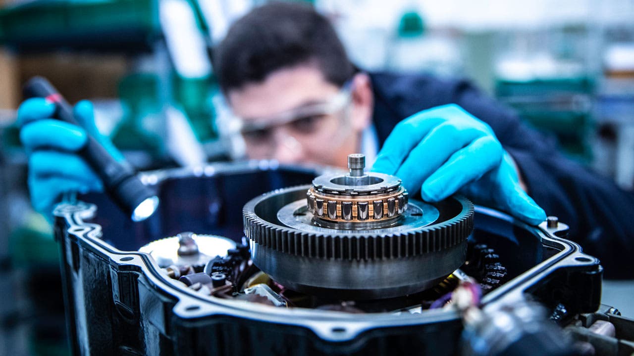 Close-up scene of a engineer inspecting a mechanical gear system. Person is wearing blue protective gloves and safety glasses.