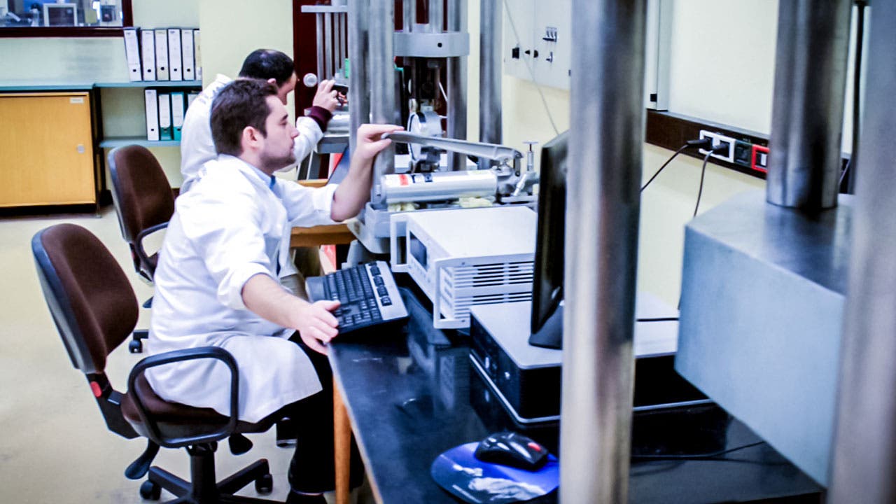 A laboratory setting with two scientists interacting with laboratory testing equipment.
