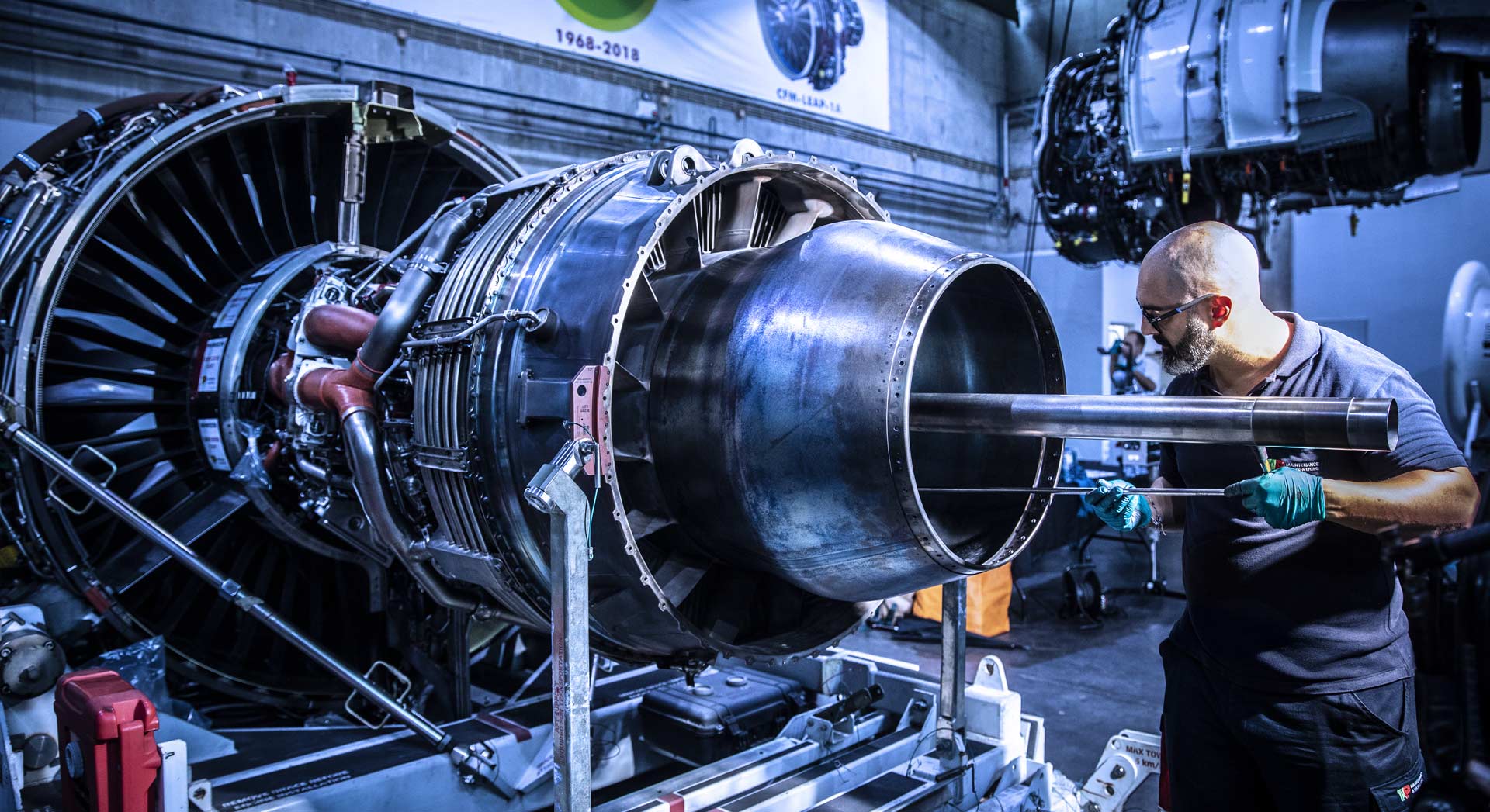 TAP Maintenance worker working on a large aircraft jet engine inside a maintenance facility.