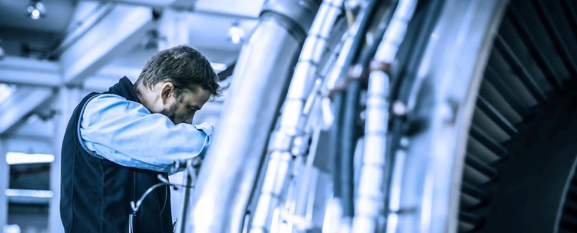 TAP Maintenance worker inspecting a large mechanical component, part of a jet engine.