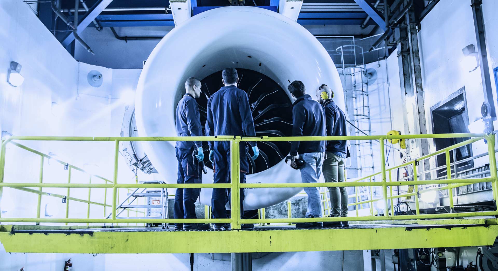 Four TAP Maintenance workers standing on a platform in front of a large jet engine.