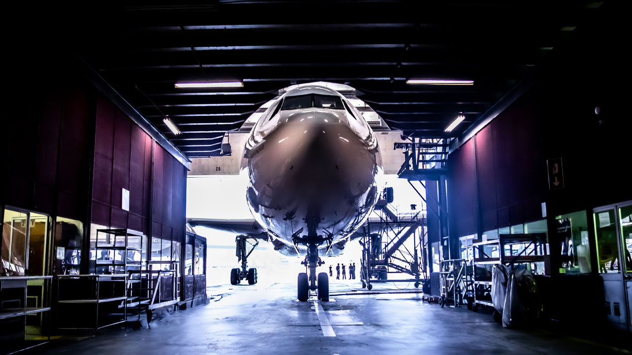 Front view of a commercial airplane inside a large maintenance hangar.